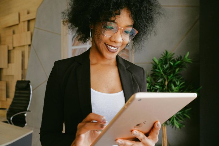 Smiling woman using a tablet in a modern office setting, showcasing technology and business.